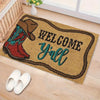 A welcome doormat featuring a cowboy boot design and the text Welcome Y'all on a light wood floor.