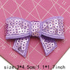 Purple sequin bow patches for DIY decoration shown on a pink grid background