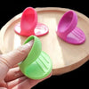 A hand holds a bright green silicone oven mitt with pink accents on a wooden cutting board.