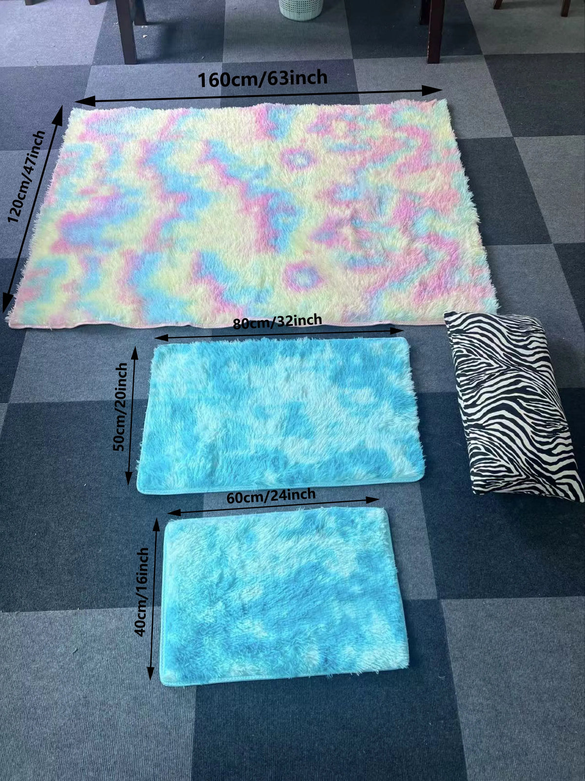 Three rectangular silk wool floor rugs in pastel blue, pink, and white are displayed on a gray checkered floor.