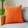 An orange ribbed corduroy cushion cover resting on a gray sofa next to a potted plant.