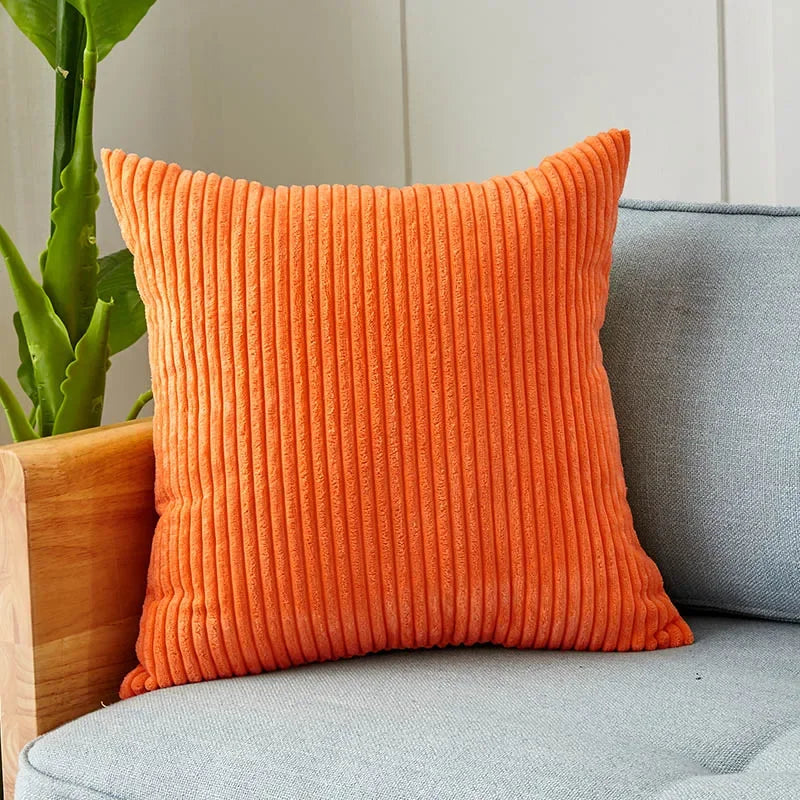 An orange ribbed corduroy cushion cover resting on a gray sofa next to a potted plant.