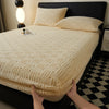 A beige plush jacquard mattress cover is shown on a black bed with matching pillows and a black and white checkered floor.