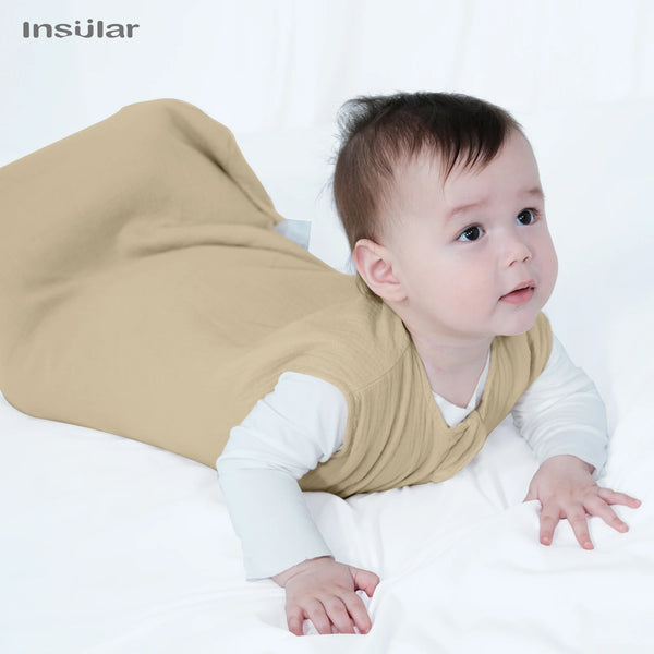 A baby wearing a beige muslin cotton sleeping bag lying on a white surface.