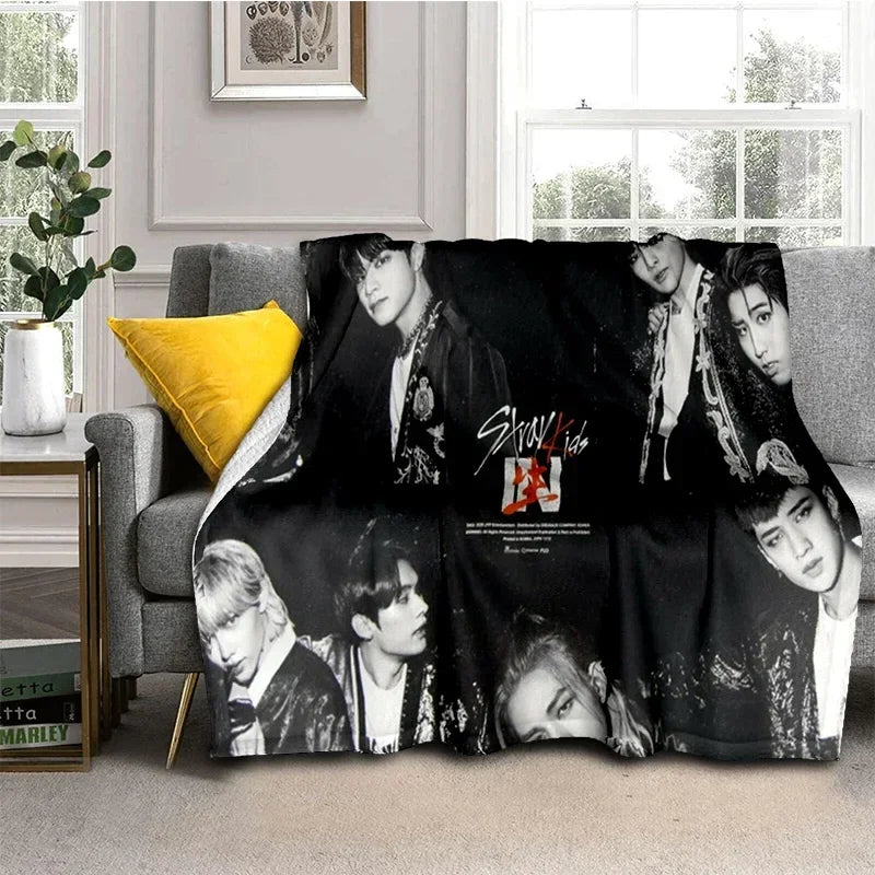 A black fleece throw blanket featuring multiple portraits of Stray Kids members.