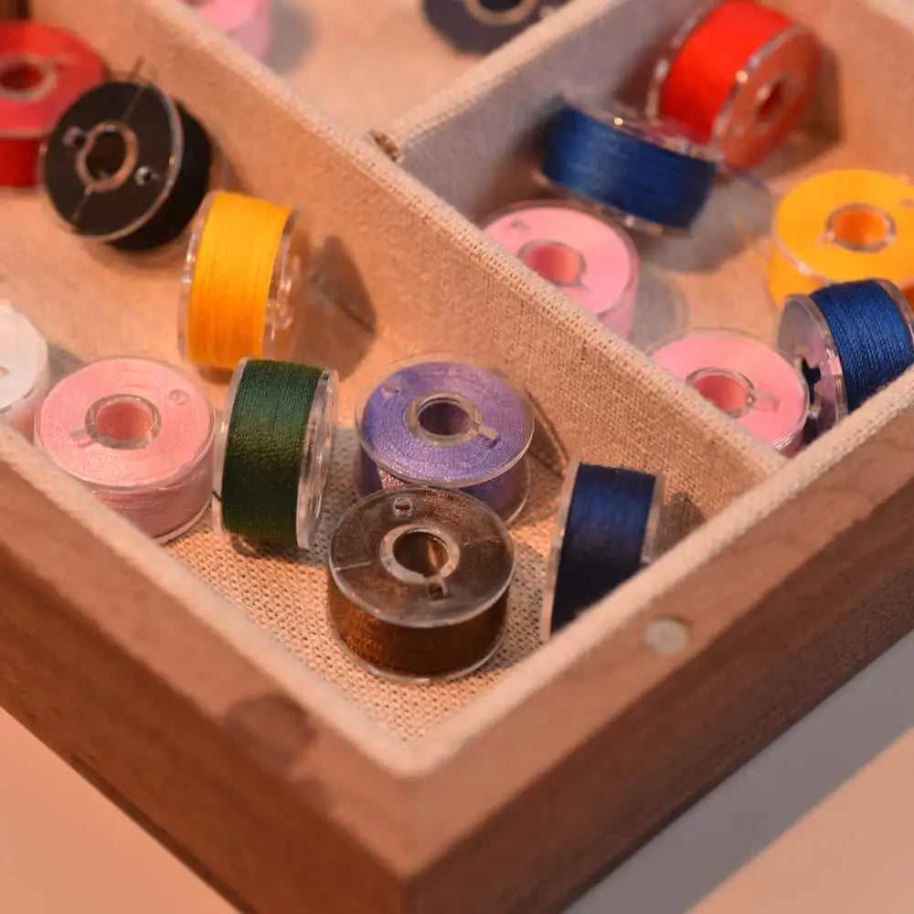 A wooden box filled with various prewound sewing machine bobbin threads in colors like orange, yellow, blue, and pink.