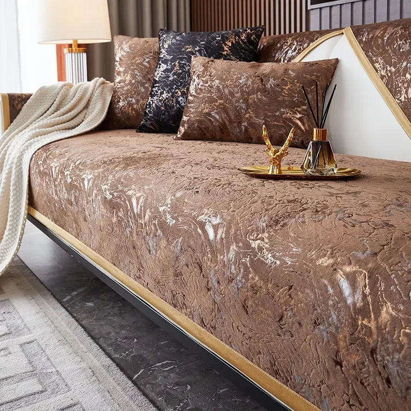 A luxurious brown velvet sofa cover with gold accents and a cream throw blanket on a modern bed.