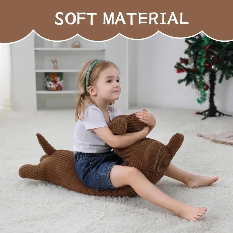 A young girl is sitting on a white rug holding a brown corduroy dachshund body pillow.