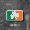 A rectangular embroidered badge featuring a green shamrock and an orange clover on a white background.