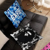 A black leather sofa features a blue and white patterned pillow cover and a black and white camouflage print pillow.