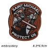 An embroidered patch featuring a winged figure holding a sword with the text SAINT MICHAEL PROTECT US on a brown background.