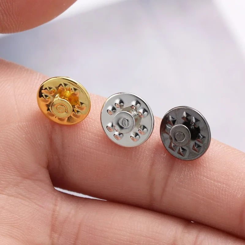 Three metal pin findings including a gold butterfly brooch clasp and two silver tie tacks are shown on a finger.