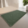 A rectangular green waffle design non-slip bathroom mat placed on a light gray floor next to a white bench.