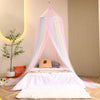A bed decorated with a rainbow mesh mosquito netting canopy and pillows in pastel colors.
