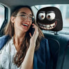 A woman smiling while holding a phone in a car interior, next to a decorative smiley face pillow cover.