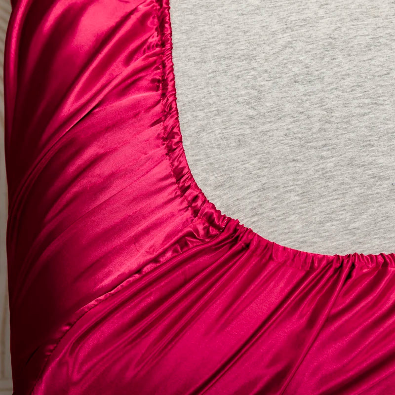 Close-up of a vibrant magenta satin bedding set with fitted sheets.