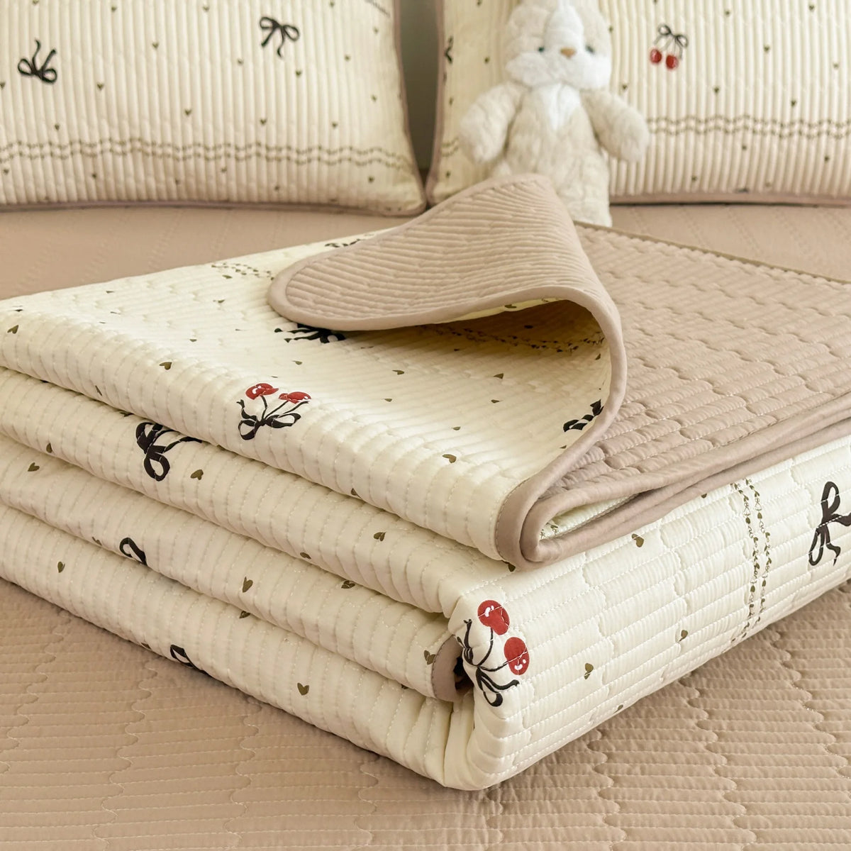 A stack of cream quilted fabric with small floral embroidery rests on a light pink surface.