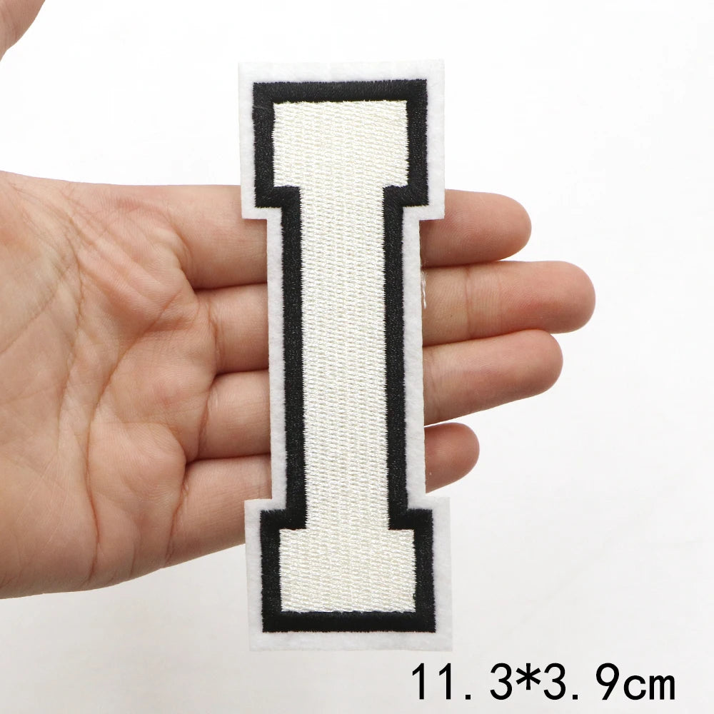 A hand holds a rectangular letter patch, the letter I, with black and white stitching.