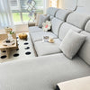 A light gray jacquard elastic sofa slipcover with textured fabric and decorative pillows in a bright, modern living room.