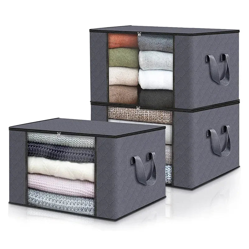 A stack of dark gray storage boxes filled with neatly folded clothing and blankets in various neutral colors.