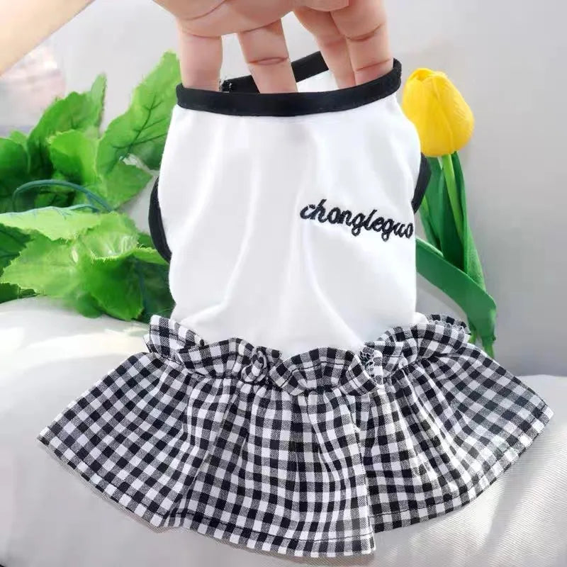White dog dress with a black and white checkered skirt and a yellow flower accessory