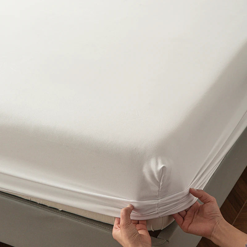 A hand is adjusting the elastic edge of a white soft touch microfiber fitted sheet on a bed.