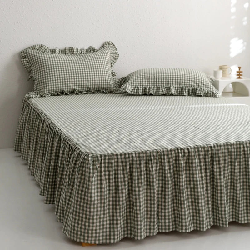 A plaid cotton bed skirt cover in olive green and cream checkered pattern draped over a bed.