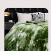 A green and white tie-dye flannel fleece throw blanket draped over a bed.