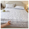 A white floral printed cotton fitted sheet is displayed on a bed with a upholstered headboard.