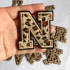 A hand holds a leopard print alphabet iron-on patch letter N and several other letters.