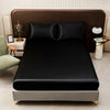 A black satin bedding set with fitted sheets displayed on a bed in a modern bedroom setting.
