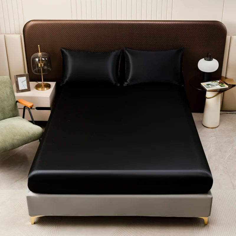 A black satin bedding set with fitted sheets displayed on a bed in a modern bedroom setting.
