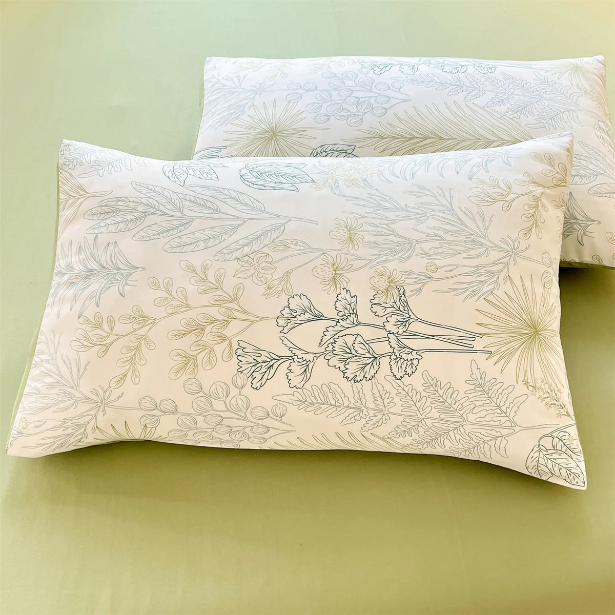 A light beige floral printed pillow cover with delicate line drawings of leaves and flowers resting on a green surface.