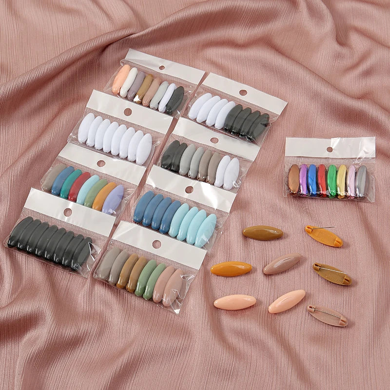 A collection of eight plastic safety pins in various neutral and pastel colors packaged in clear plastic sleeves.