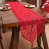 A vibrant red lace table runner with tassels is displayed on a wooden table.