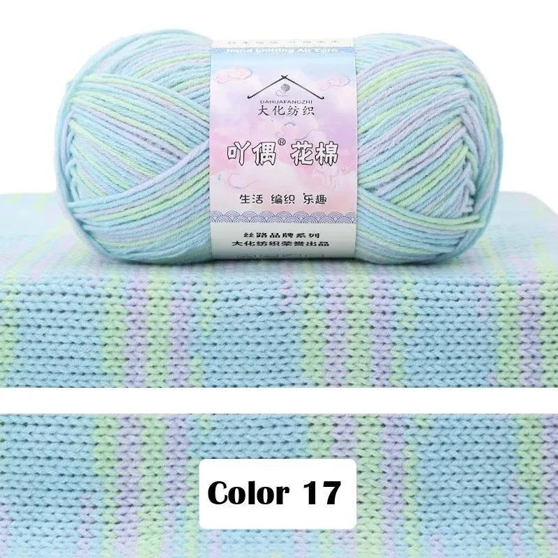 A ball of light blue and green gradient colored 4-ply cotton knit yarn is displayed on a textured surface.