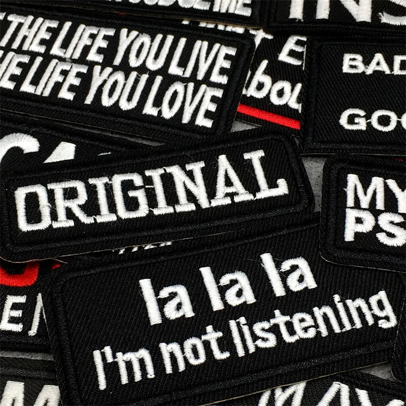 A collection of black embroidered patches with white text featuring phrases like THE LIFE YOU LIVE and ORIGINAL.