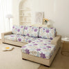 A beige sofa covered with a floral print elastic protective cover in purple and blue tones.