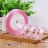 Pink satin ribbon rolled on a disk next to green foliage.