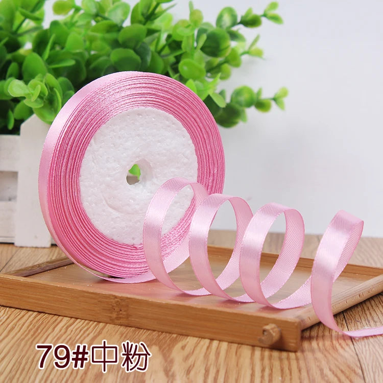Pink satin ribbon rolled on a disk next to green foliage.