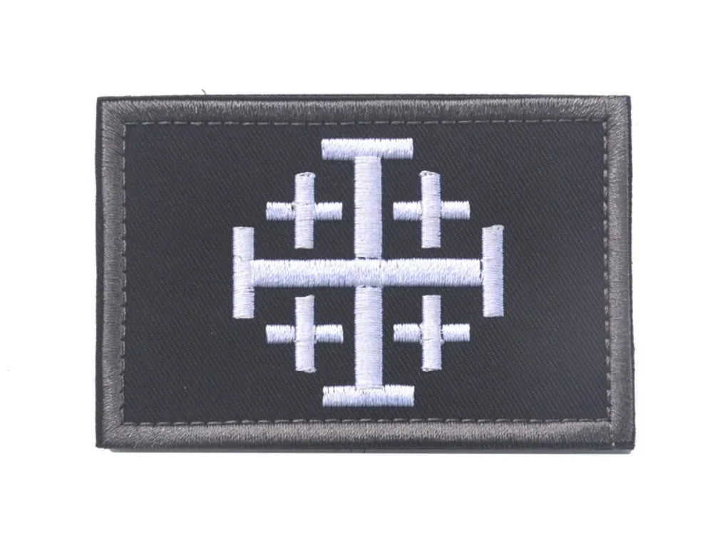 A black embroidered patch featuring a white stylized cross design.
