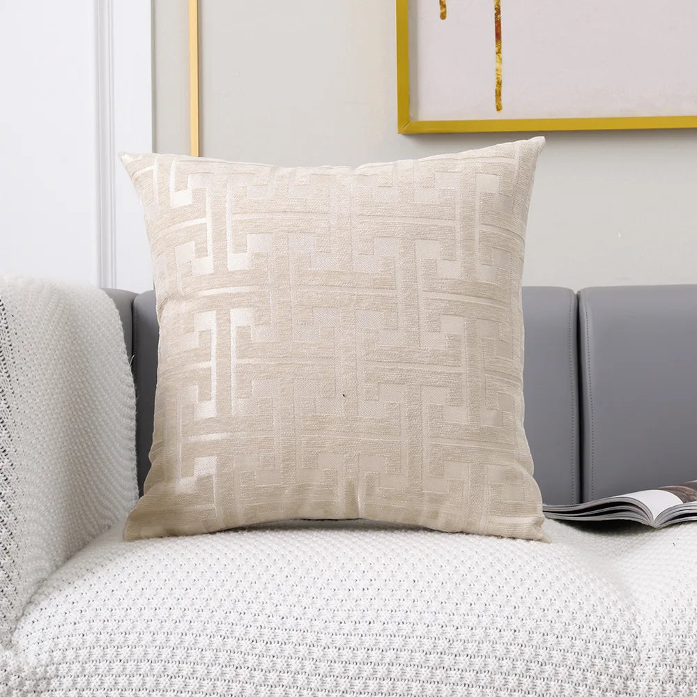 A beige geometric jacquard lumbar pillow cover resting on a gray sofa and white textured fabric.
