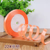 Roll of orange satin ribbon with a white center, displayed on a wooden board.