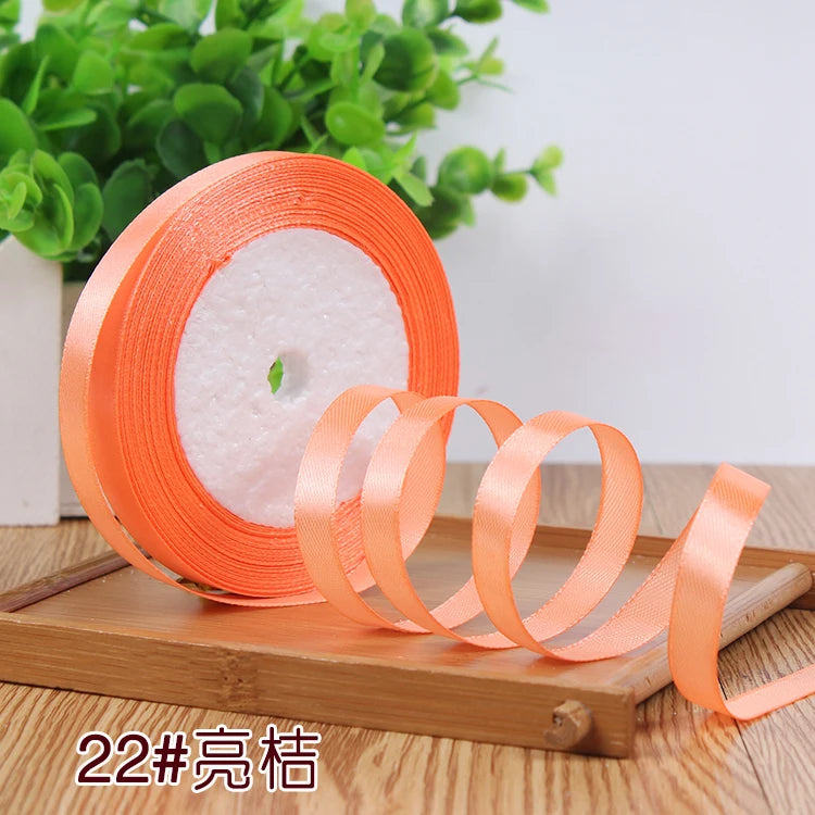 Roll of orange satin ribbon with a white center, displayed on a wooden board.