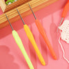 A set of orange and yellow aluminum plastic crochet hooks displayed on a pink background.