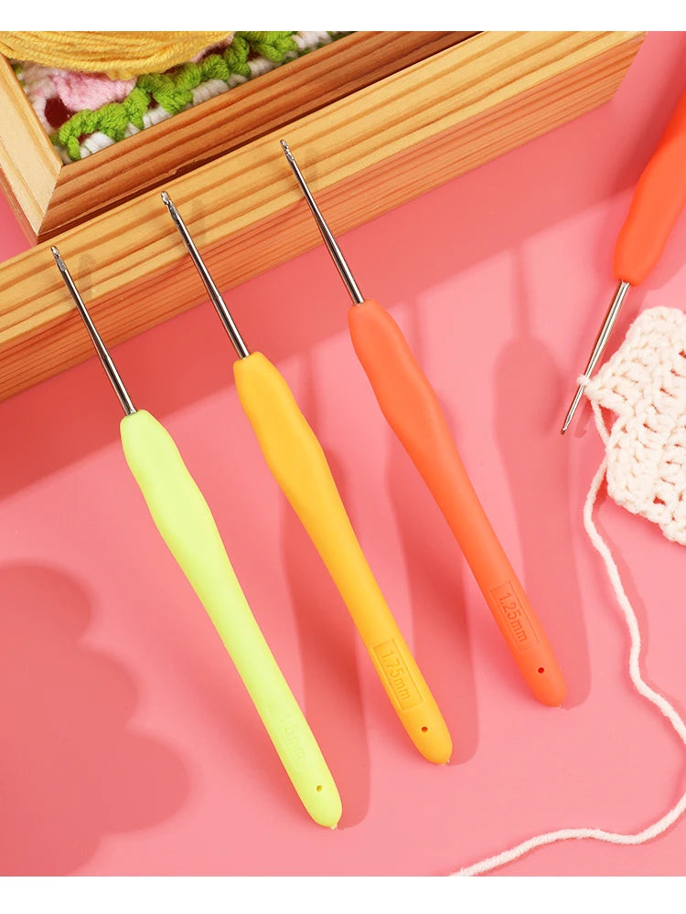 A set of orange and yellow aluminum plastic crochet hooks displayed on a pink background.