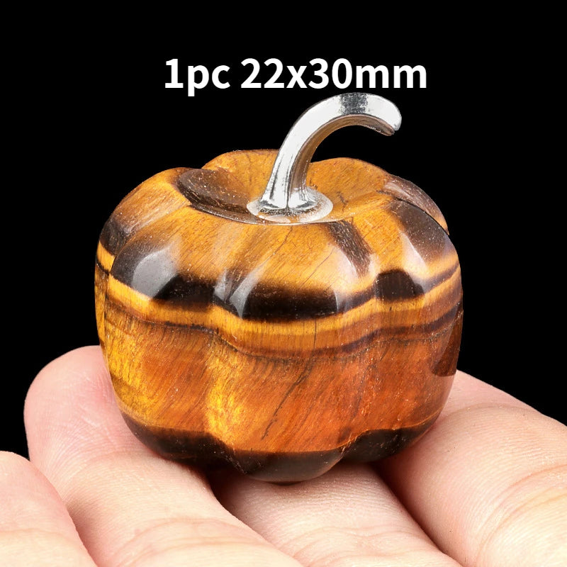 A handcrafted natural stone pumpkin figurine with a silver-colored stem is held in a person's hand.
