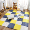 A yellow, white, and blue checkered foam play mat is laid on a wooden floor with a framed cat artwork nearby.