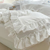 A white ruffled duvet cover set displayed on a bed with a framed photo.