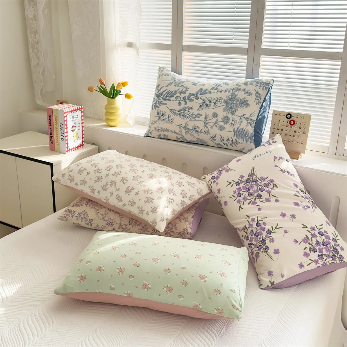 A collection of floral printed pillow covers in shades of blue, purple, and pink displayed on a white surface.